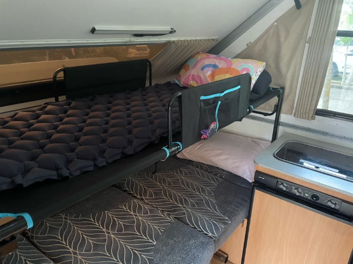 Spinifex bunk set up over the bench bed in a 1D Avan Cruiseliner, with a sleeping pad on the top bunk next to the kitchenette