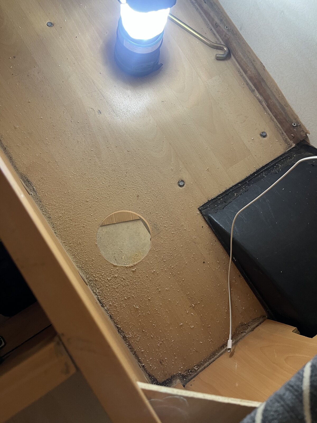 Completed circular cutout in caravan floor timber with work light illuminating cabinet