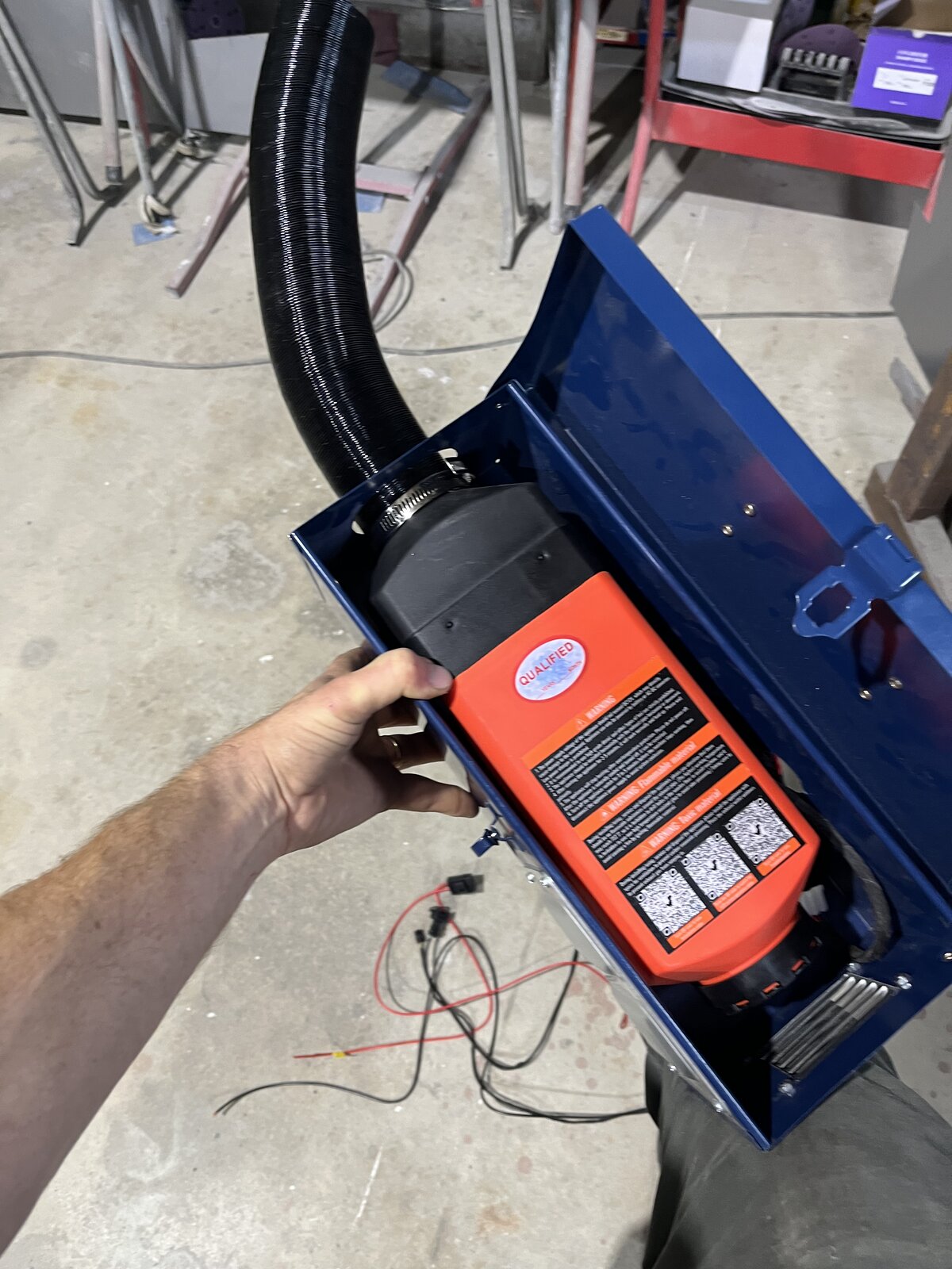 Vevor diesel heater being lowered into the blue steel enclosure with exhaust hose attached