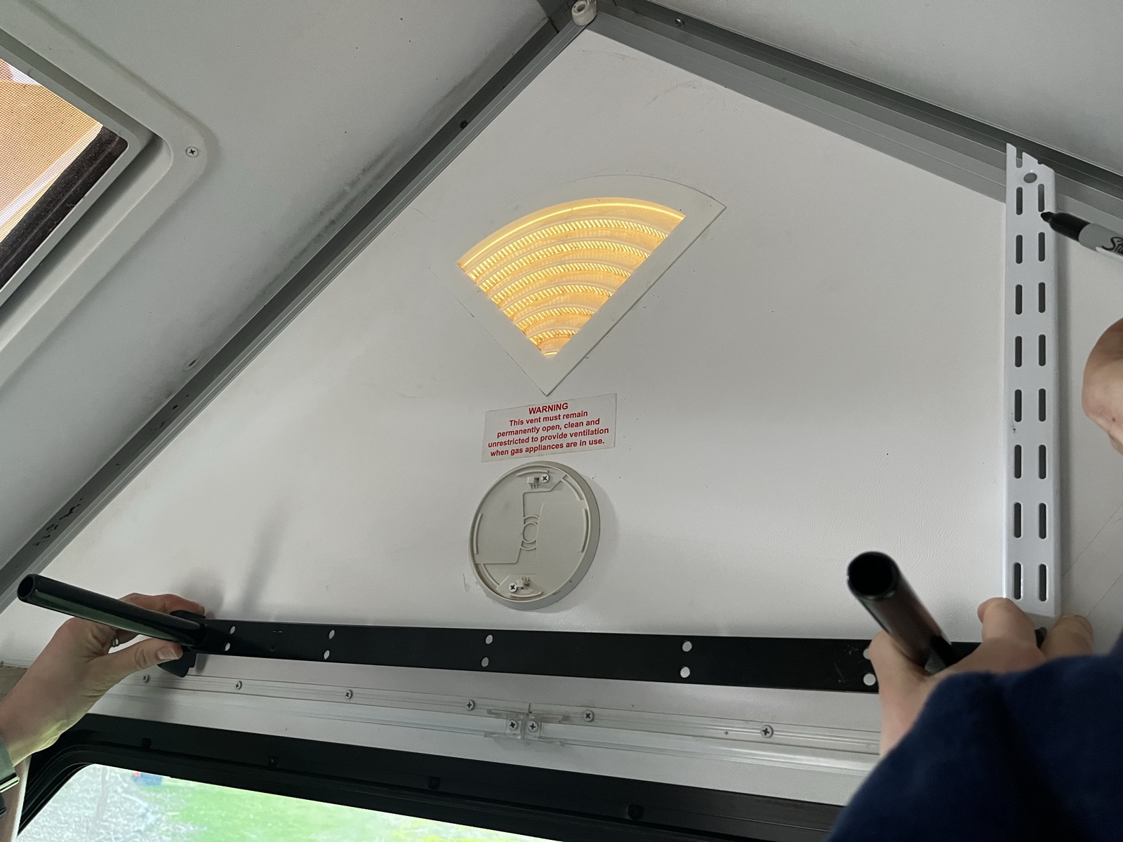 Holding a wall strip against the angled apex panel to mark the length and shelf position above the curtains